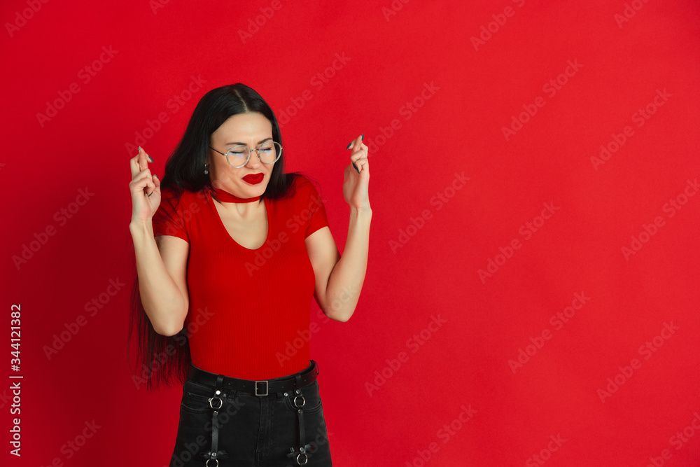 Praying for good luck. Caucasian young woman's monochrome portrait isolated on red studio background. Beautiful female brunette model. Concept of human emotions, facial expression, sales, ad.