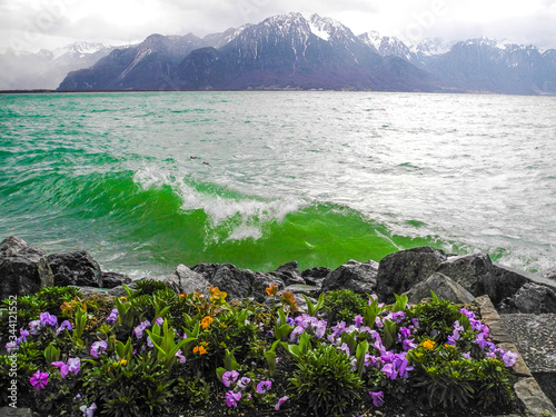 Fantastic panorama of lake and Alpine mountains. Bright green water, colorful flowers.