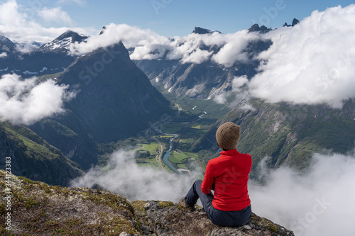 A woman traveller sitting and looking to mountains in Romsdalseggen hiking trail, Norway, Scandinavia