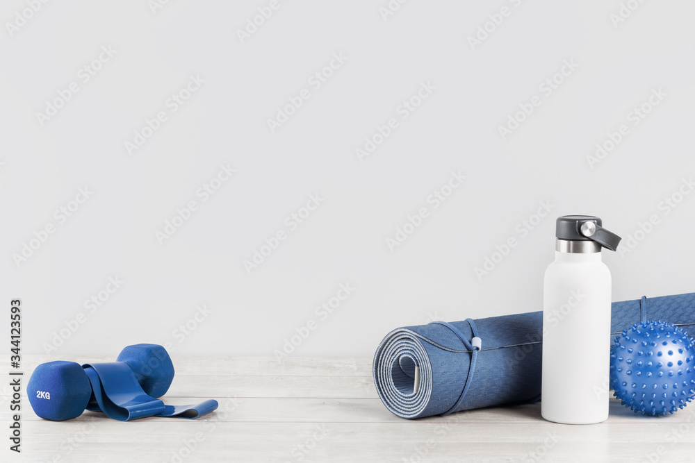 Rolled blue yoga mat and white metal water bottle flask grey