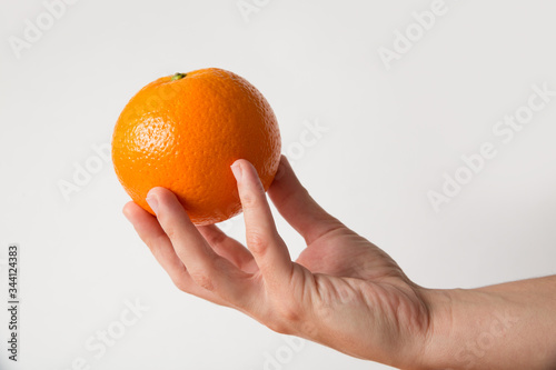 Unrecognizable person holding orange fruit in hand with fingers. Cropped shot, side view, isolated on white. Healthy nutrition or organic food concept