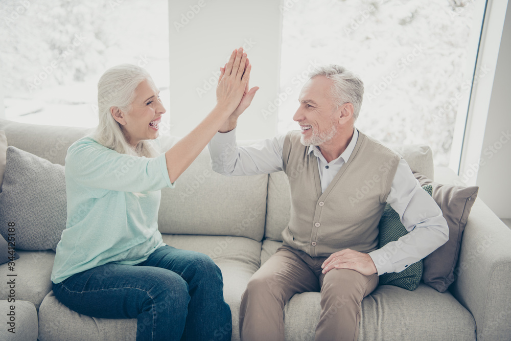 Portrait of lovely grandparents giving high five enjoying wearing teal brown jumpers trousers jeans sitting divan room Portrait of lovely grandparents giving high five enjoying wearing teal brown jumpers trousers jeans sitting divan room