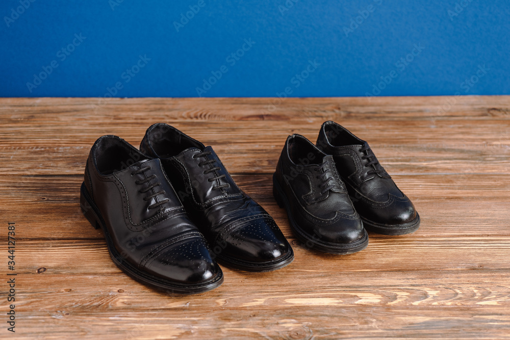 High angle view of black mens and childrens shoes isolated on blue, fathers day concept High angle view of black mens and childrens shoes isolated on blue, fathers day concept