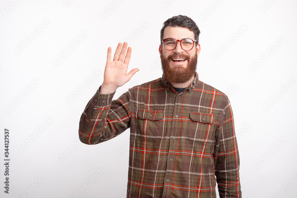 Young bearded man smiling at the camera is showing hello gesture presenting himself to the world on white background.