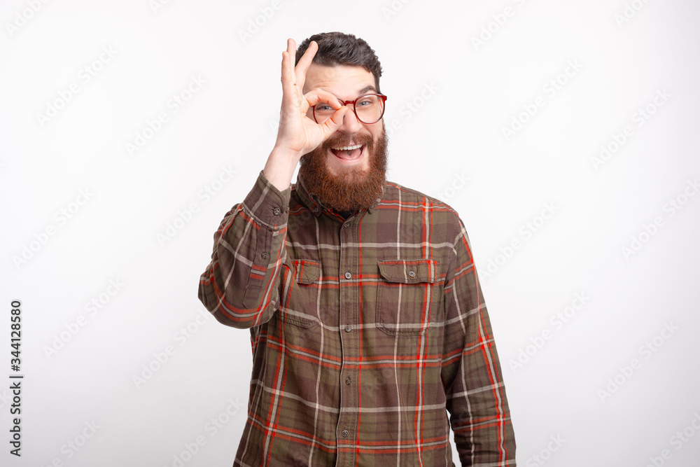 Smiling mature man wearing glasses is looking through ok gesture on white background. Smiling mature man wearing glasses is looking through ok gesture on white background.