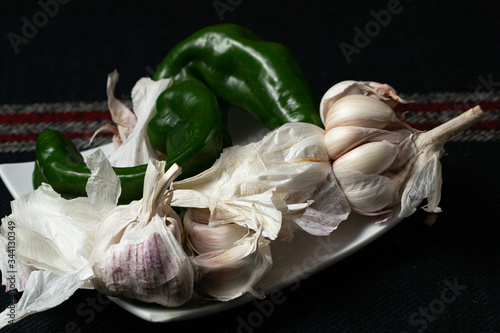 Cabezas de ajos y pimientos verdes sobre bandeja blanca en fondo negro