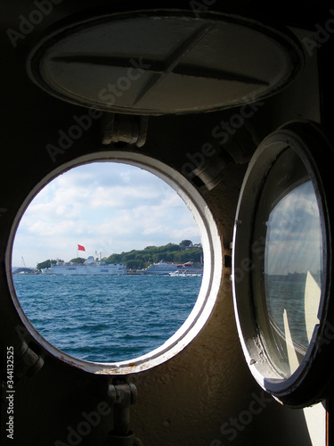 View from the ship’s cabin through a round porthole, on a green sea island. Sea transport concept. Transportation of people by sea © Kate