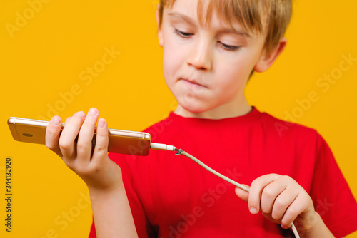 Boy holding a mobile phone with a defective charging cord. Boy thinks how to repair cabel.