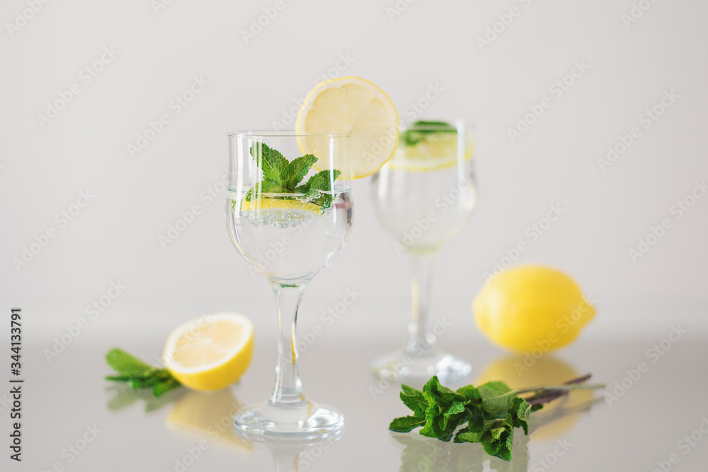 Two glasses of mineral water with lemon and fresh mint on glass surface. Sparkling drink with citrus and herbs