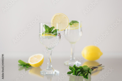 Two glasses of mineral water with lemon and fresh mint on glass surface. Sparkling drink with citrus and herbs
