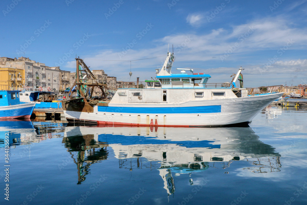 Fishing boat with its reflection in the sea moored in the port of the historic center of Taranto, Puglia, Italy