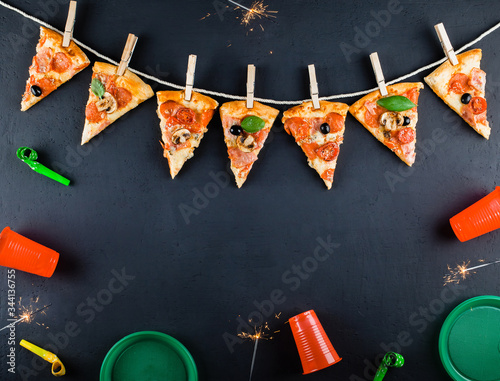 Slices of pizza in the form of a garland with the attributes of a party and Bengal Candles. Pizza slices on a gray concrete background. Space for text. Pizza menu. Birthday with fast food. 