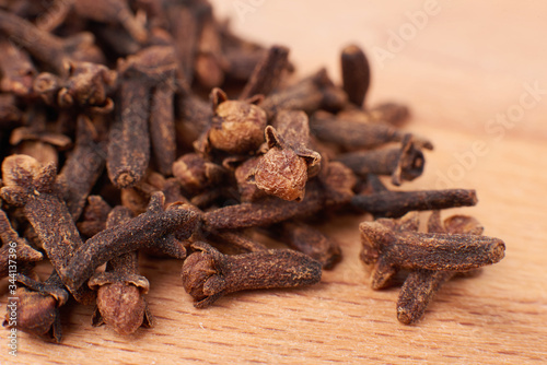A spice of dried cloves lies on a wooden spoon and is scattered on old wooden boards near the bag. Spices cloves for cooking. Close-up.