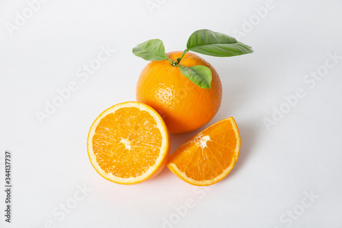 Whole orange and cut fruit pieces with green leaves isolated on white background. Closeup shot. Natural vitamin or organic food concept