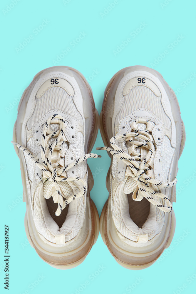 Pair of new trendy beige sneakers isolated on a light blue background with shadow. Top view. Pair of new trendy beige sneakers isolated on a light blue background with shadow. Top view.