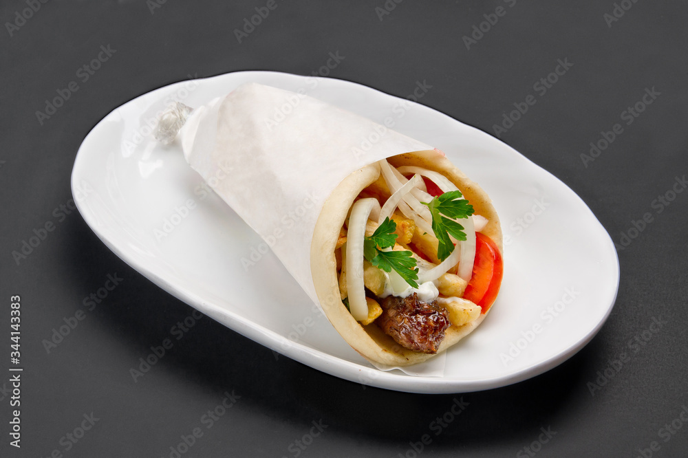 Meat, French fries and vegetables wrapped in pita with sauce on white ceramic plate on grey background Meat, French fries and vegetables wrapped in pita with sauce on white ceramic plate on grey background