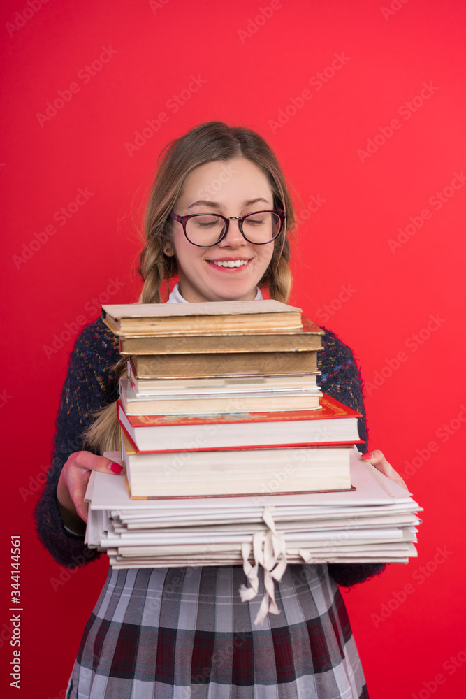 Schoolgirl teenager with pigtails and glasses, in a checkered skirt, on a red background and holds a bunch of books, vertical Schoolgirl teenager with pigtails and glasses, in a checkered skirt, on a red background and holds a bunch of books, vertical