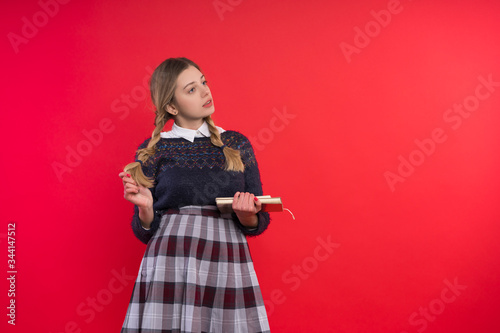 schoolgirl teen with two pigtails in a jumper and checkered skirt with a book in hand on a red background