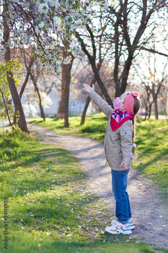 Little girl wearing pink protective face mask against COVID-19 coronavirus disease on the nature with blooming trees during quarantine.Stop epidemic.Pretty child in surgical protection on empty street