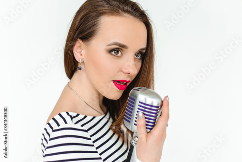 A girl with red lipstick holds a retro microphone and sings on white background. The isolated portrait.