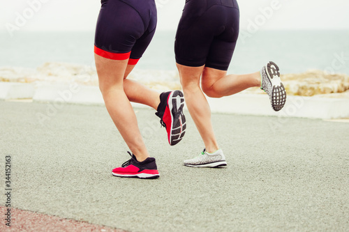Cropped shot of women running on sea shore. Low section of athletic women in sportswear jogging near body of water at cloudy day. Triathlon concept