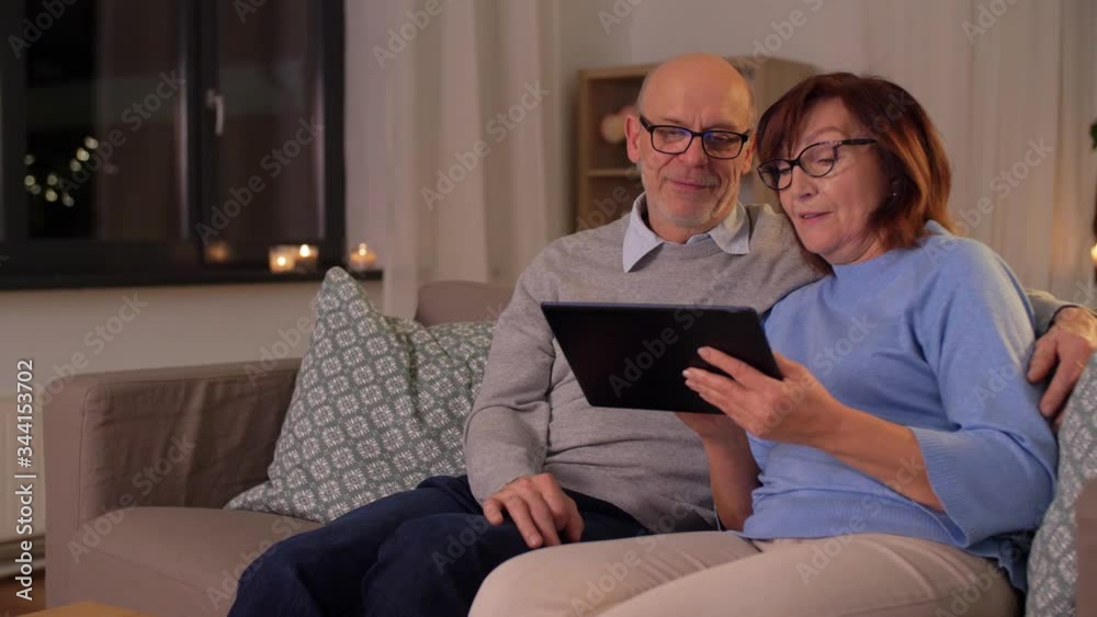 technology, old age and people concept - happy smiling senior couple with tablet pc computer at home in evening technology, old age and people concept - happy smiling senior couple with tablet pc computer at home in evening