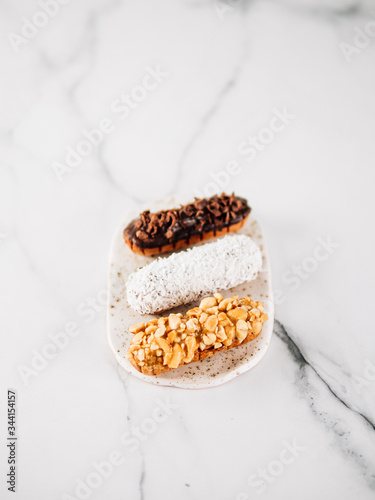 Set of three homemade eclairs on marble background. Top view of delicious healthy profitroles with different decor elements - chocolate, peanut and sherdded coconut. Vertical photo