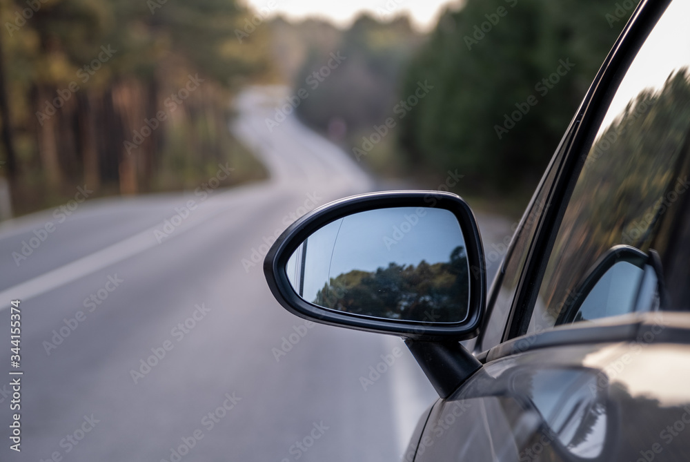 Car rear view mirror on wooded rural road. Driving car