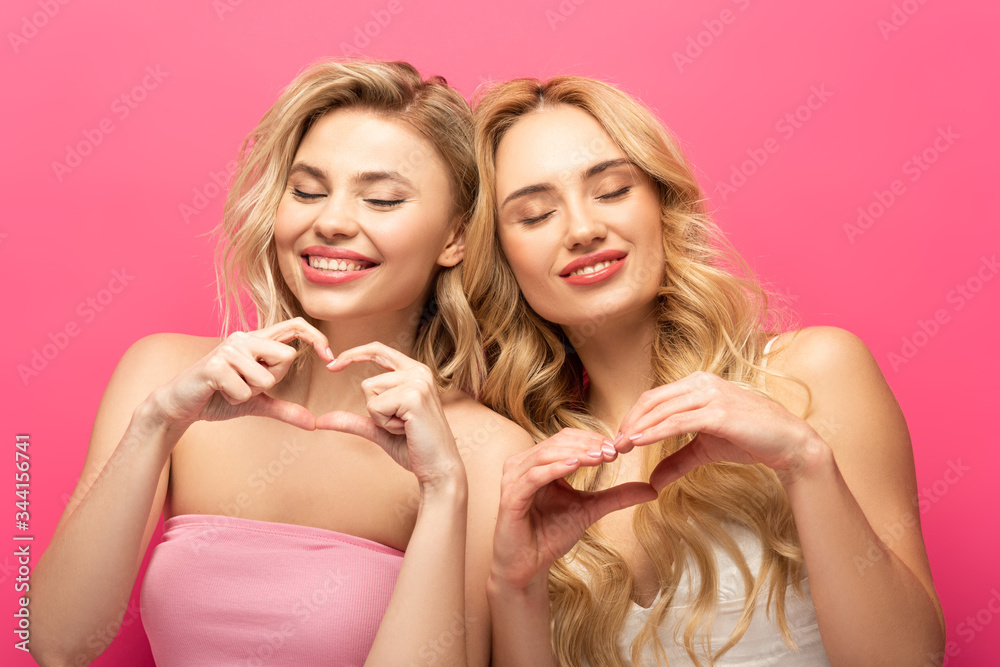 Smiling blonde girls with closed eyes showing heart sign on pink background Smiling blonde girls with closed eyes showing heart sign on pink background