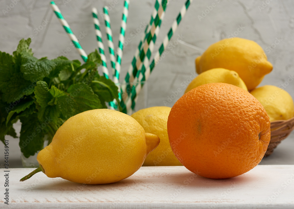 whole orange, yellow ripe lemon and a bunch of mint on a wooden board