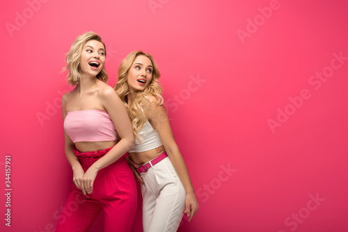 Positive blonde friends looking away on pink background