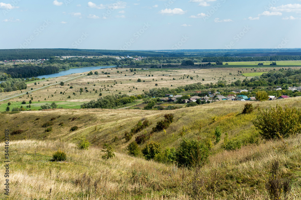 Obraz premium Rural landscape with rustic homes, fields of wheat, sheafs and river