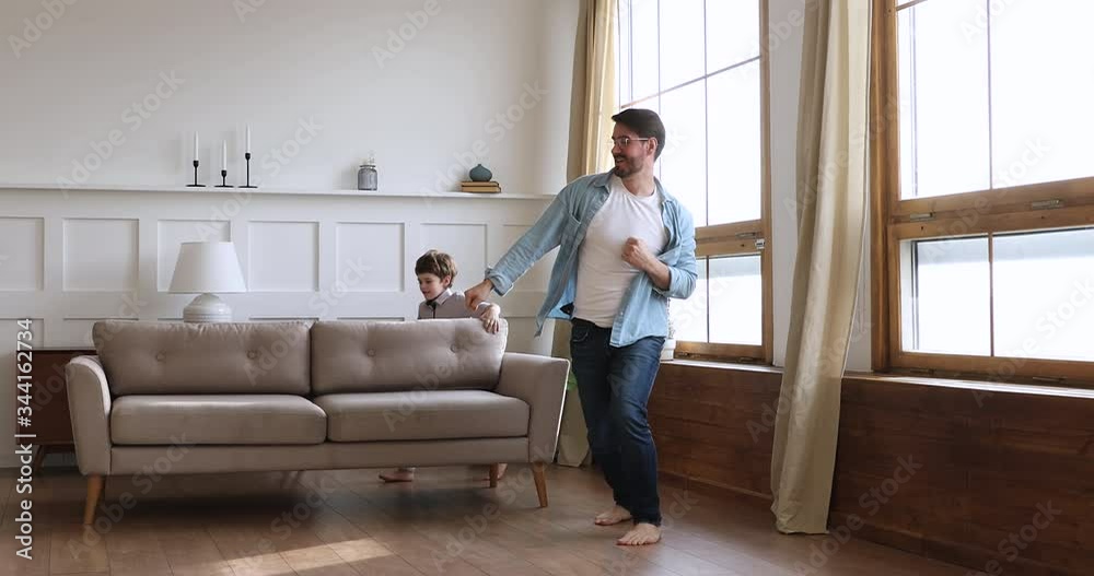 Full length overjoyed young father dancing barefoot on heated wooden floor with small joyful child son. Happy energetic little kid boy running, having fun with playful daddy in modern living room. Full length overjoyed young father dancing barefoot on heated wooden floor with small joyful child son. Happy energetic little kid boy running, having fun with playful daddy in modern living room.