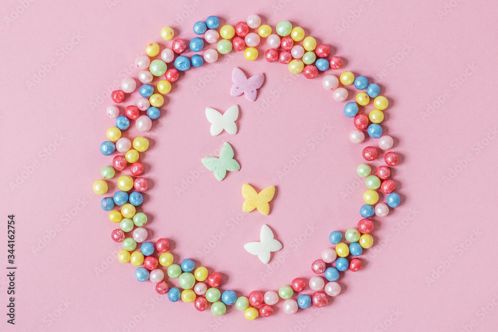 Pastry sprinkles are scattered in the form of a circle, inside it are enclosed colorful butterflies on a pink background