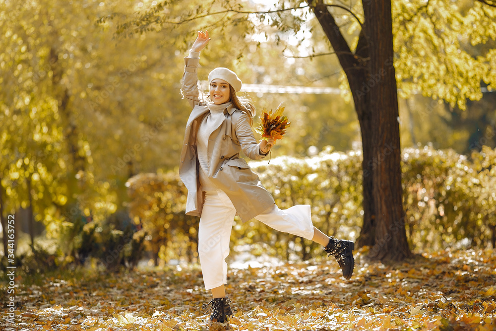 Fototapeta premium Girl in a brown coat. Woman in a autumn park. Lady with a leaf.