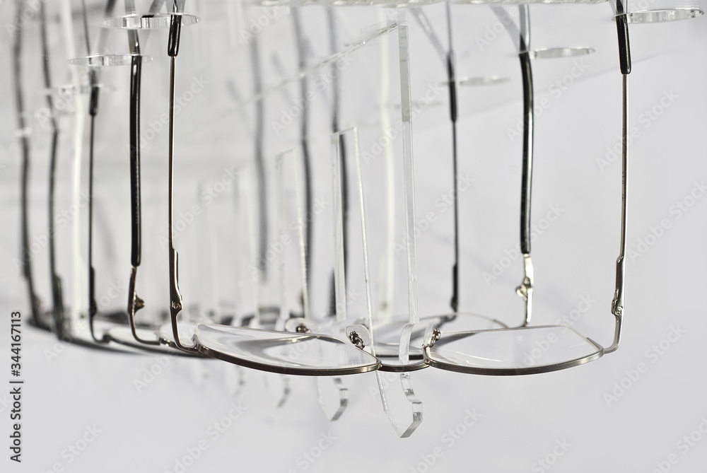 Many glasses on a white background. Glasses are stacked in a row on a transparent shop window. Glass stand on gray table. Sale and exhibition of optics. Many glasses on a white background. Glasses are stacked in a row on a transparent shop window. Glass stand on gray table. Sale and exhibition of optics.