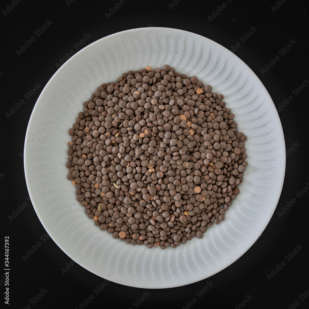 Uncooking lentils in a white plate on black background Uncooking lentils in a white plate on black background