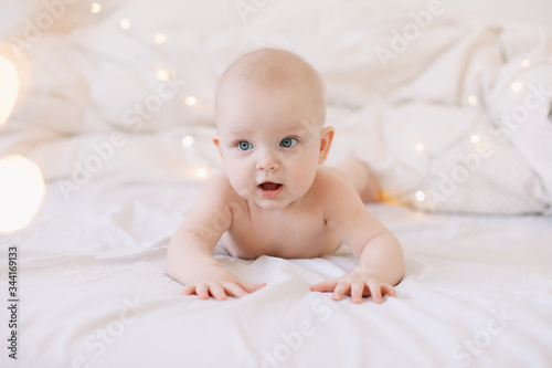 Little child doing tummy time. Adorable baby learning to crawl in white  bedroom. Cute funny baby lying on bed. 