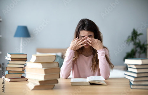 Upset young woman with books sit at work desk.