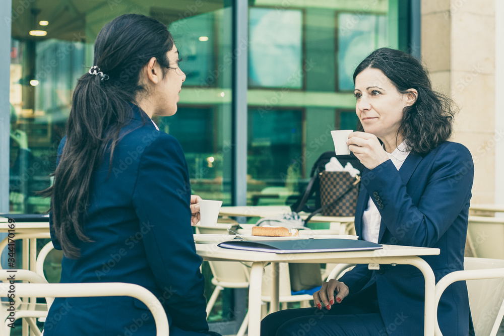 © Mangostar - Businesswomen drinking coffee in outdoor cafe. Female colleagues in formal wear sitting at table and drinking coffee together. Coffee time concept © Mangostar - Businesswomen drinking coffee in outdoor cafe. Female colleagues in formal wear sitting at table and drinking coffee together. Coffee time concept