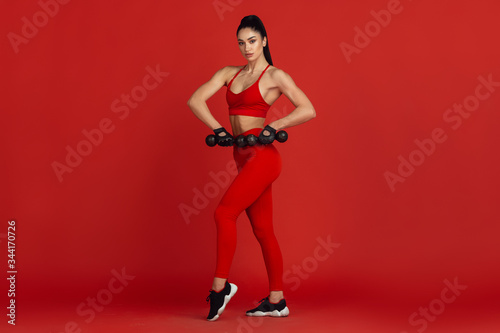 Graceful. Beautiful young female athlete practicing in studio, monochrome red portrait. Sportive fit brunette model with weights. Body building, healthy lifestyle, beauty and action concept. © master1305