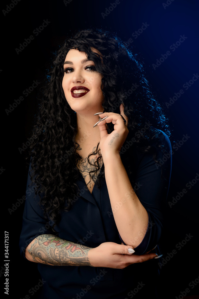 Portrait of a beautiful brunette girl with a tattoo in a dark dress against a black background with blue highlighter Portrait of a beautiful brunette girl with a tattoo in a dark dress against a black background with blue highlighter