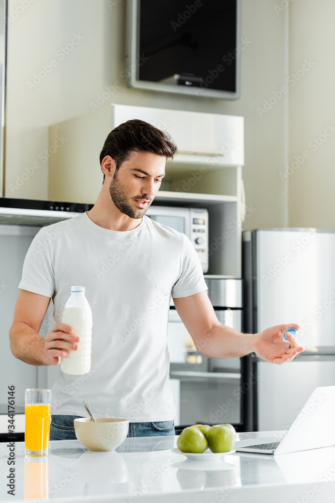 Man holding bottle of milk while having video chat on laptop in kitchen Man holding bottle of milk while having video chat on laptop in kitchen