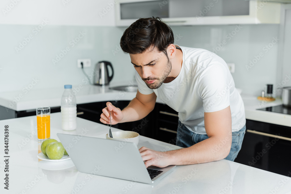 Handsome man using laptop during breakfast on table in kitchen Handsome man using laptop during breakfast on table in kitchen