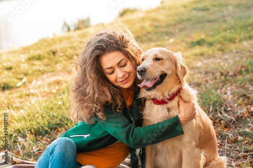 Smiling woman hugging her pet golden retriever dog near face. Golden retriever dog playing with a curly woman walking outdoors sunny day. love and care for the pet.