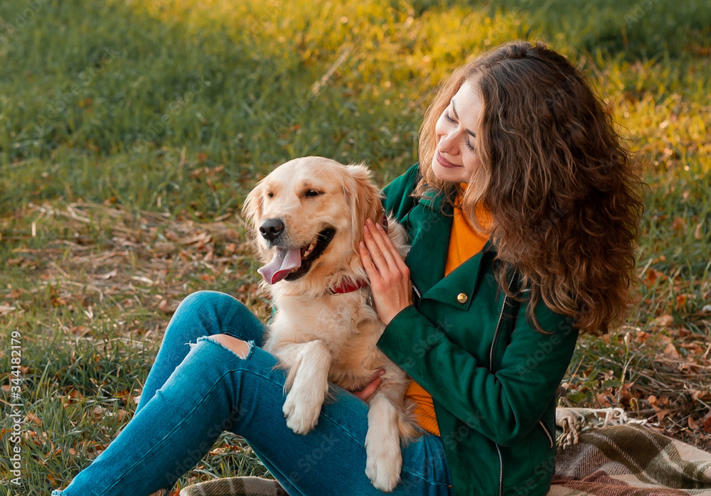 Smiling woman hugging her pet golden retriever dog near face. Golden retriever dog playing with a curly woman walking outdoors sunny day. love and care for the pet. Smiling woman hugging her pet golden retriever dog near face. Golden retriever dog playing with a curly woman walking outdoors sunny day. love and care for the pet.