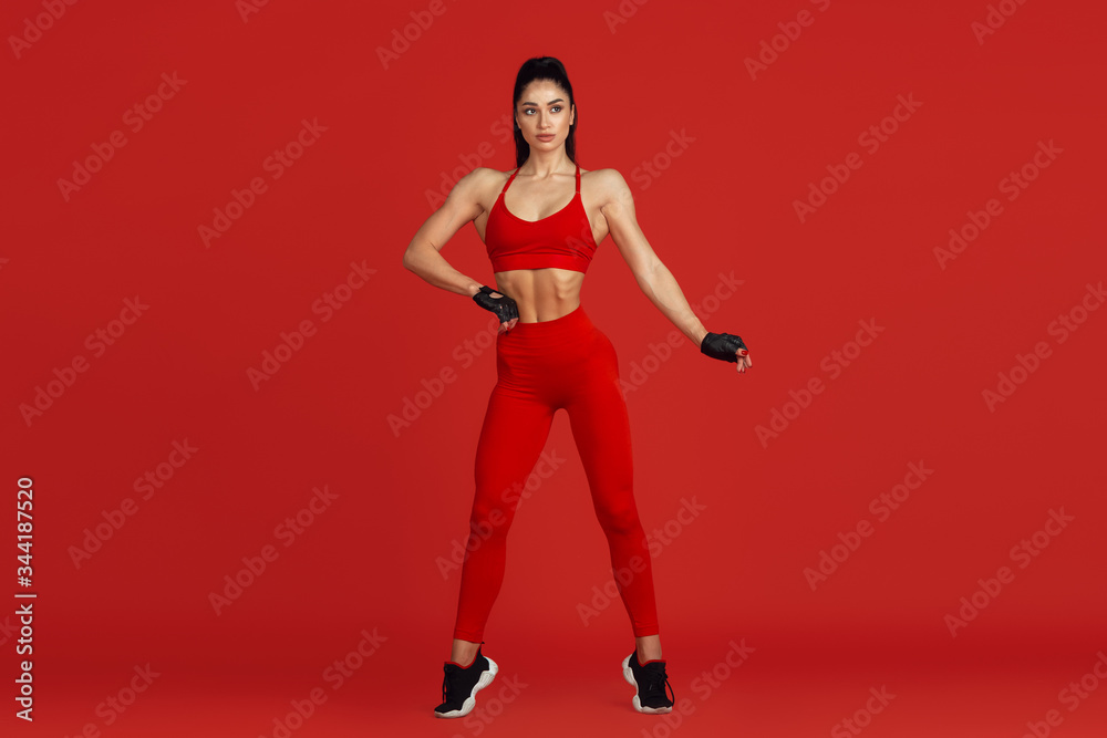 Posing graceful. Beautiful young female athlete practicing in studio, monochrome red portrait. Sportive fit brunette model training. Body building, healthy lifestyle, beauty and action concept.