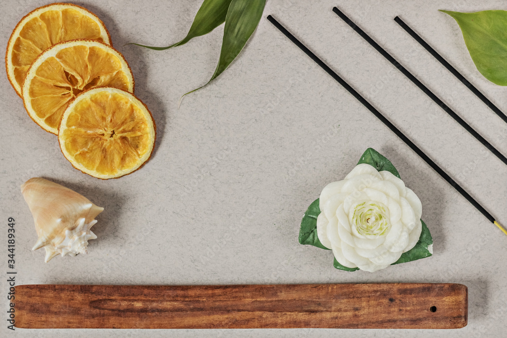 Incense sticks with a stand, sliced orange circles in a wooden bowl on a gray background. Also a candle in the form of a flower and a seashell.Aromatherapy. The concept of home Spa