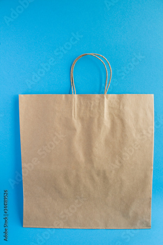 Empty paper bag for shoopping or delivery of goods on the blue background. Location vertical. Copy space.