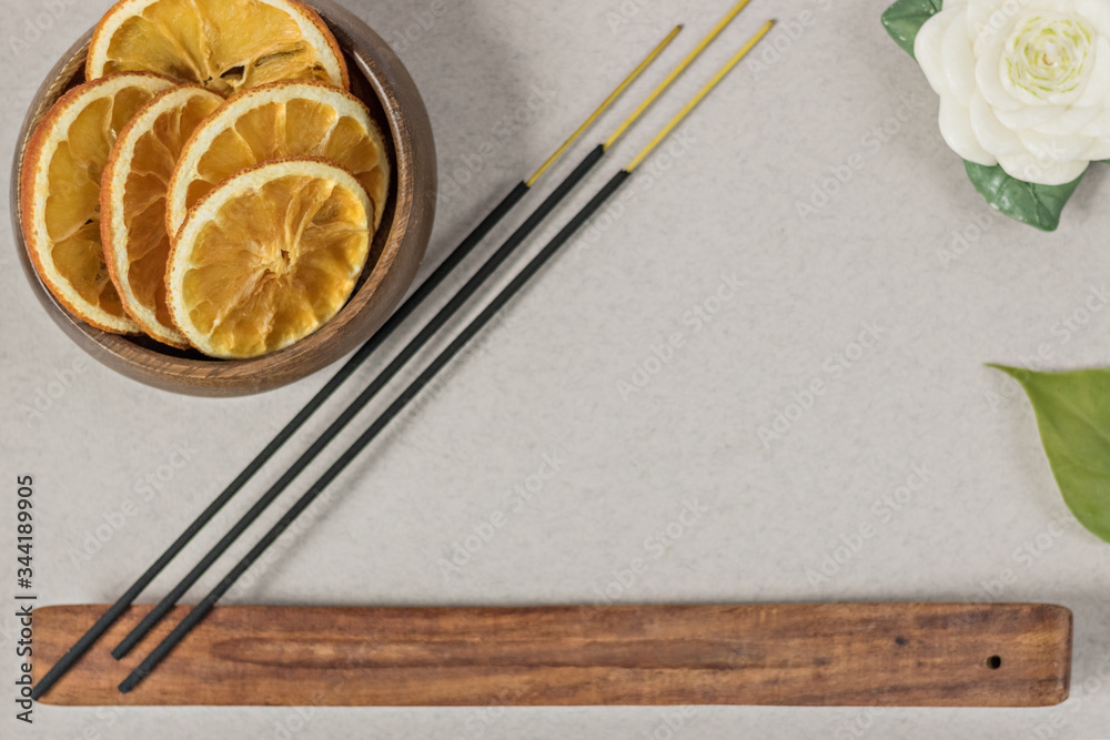 Incense sticks with stand, sliced in orange circles in a wooden bowl and anise star, cinnamon sticks on a gray background.Candle in the form of a flower and a shell.Aromatherapy. Home spa concept Incense sticks with stand, sliced in orange circles in a wooden bowl and anise star, cinnamon sticks on a gray background.Candle in the form of a flower and a shell.Aromatherapy. Home spa concept